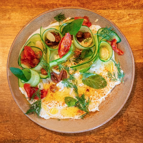 A vibrant dish with cucumber ribbons, sun-dried tomatoes, herbs, and olive oil on a bed of yogurt.