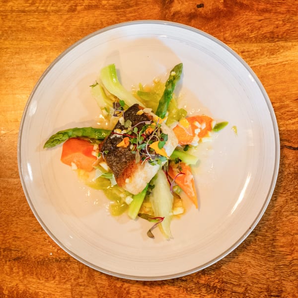 Pan-seared fish with crispy skin, asparagus, and diced vegetables on a white plate.