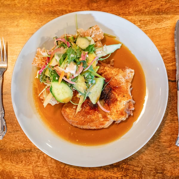 Crispy fried chicken in a rich sauce, topped with a fresh salad of greens, cucumbers, and red onions.
