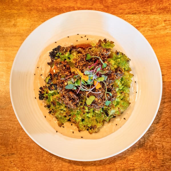 Roasted Romanesco broccoli with crispy topping, microgreens, and sauce on a white plate.