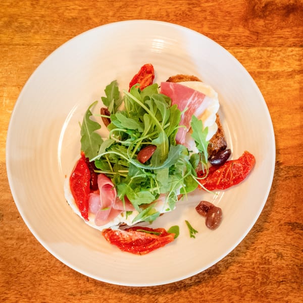 Bruschetta with prosciutto, arugula, sun-dried tomatoes, and olives on a white plate.