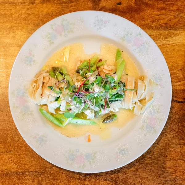 Pasta dish with wide noodles, green vegetables, microgreens, and a creamy sauce on a floral plate.