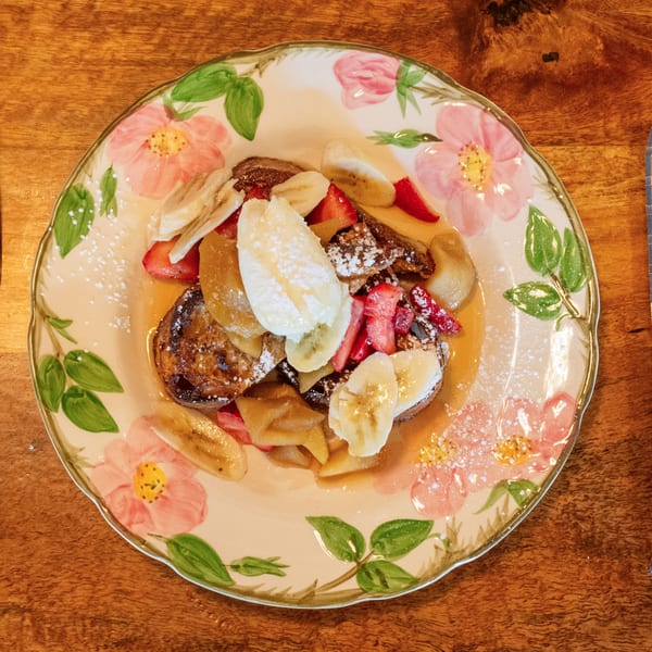 French toast topped with bananas, strawberries, powdered sugar, and syrup on a floral plate.
