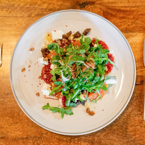 A vibrant salad with arugula, grapefruit, goat cheese, and nuts on a white plate.