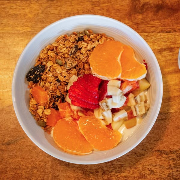 Overhead view of a breakfast bowl with granola, mandarin oranges, strawberries, and diced fruit.