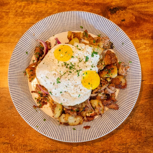 Breakfast plate with two fried eggs, crispy potatoes, and red onions on a patterned plate.