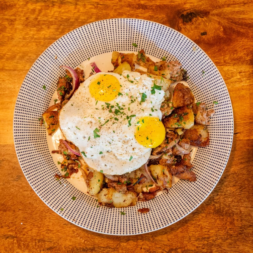Breakfast plate with two fried eggs, crispy potatoes, and red onions on a patterned plate.